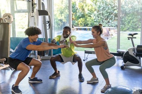 Multiethnic group performing squats in bright home gym with trainer leading workout