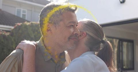 Sunlit mature couple embracing on outdoor front porch celebrating with yellow color powder