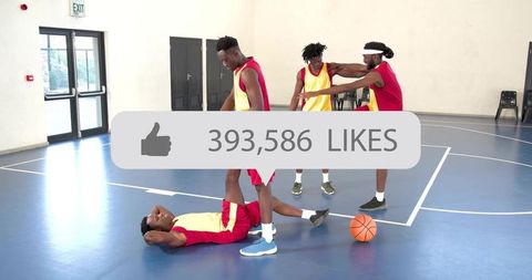 Teammates helping injured player during indoor basketball scrimmage with likes overlay