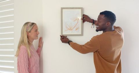 Couple hanging minimalist art on wall near window