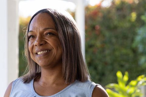 African american mature woman smiling on sunlit porch wearing blue sleeveless top, relaxed portrait