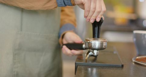 Barista tamping espresso grounds with tamper and portafilter on countertop workstation cafe