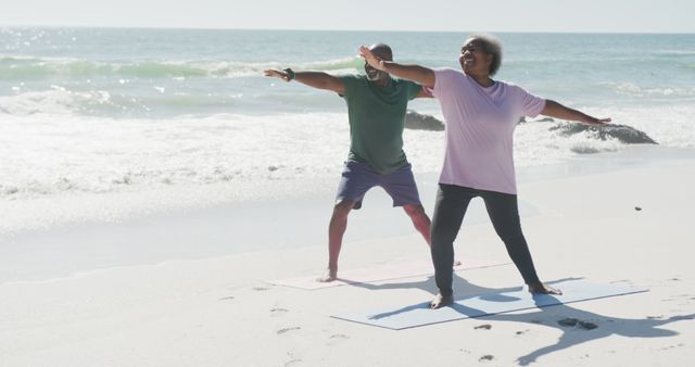 Smiling senior couple practicing yoga on the beach near ocean waves. Ideal for promoting healthy lifestyle, exercise routines, senior wellness programs, and beach vacation activities. Could be used in brochures, websites, or social media posts related to health, fitness, or travel.
