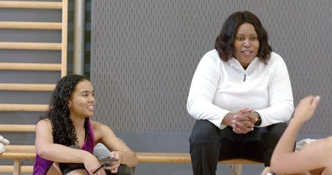 African american coach mentoring female athletes on bench in gym, teamwork motivation