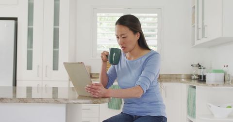 Asian Woman Relaxing with Coffee and Tablet in Kitchen - Download Free Stock Images Pikwizard.com