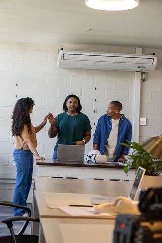 Diverse team collaborating around laptop and vr headset at bright modern coworking meeting