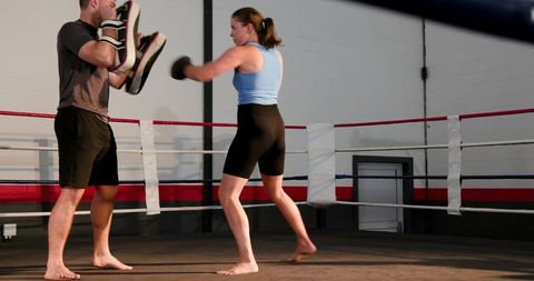 Female athlete training with coach holding focus mitts in boxing ring