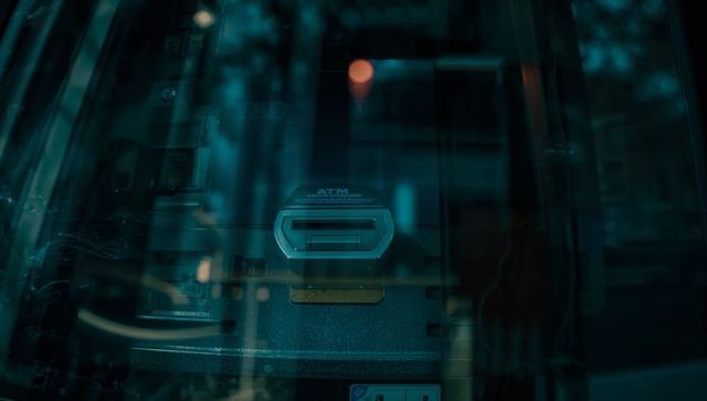 Atm card slot reflecting teal storefront glass with bokeh streetlight highlights at night
