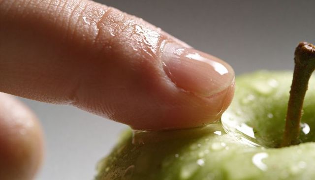 Wet fingertip pressing glossy green apple surface with water droplets macro