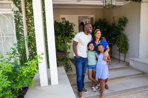 Happy Family Standing on Porch with Greenery and Smiling