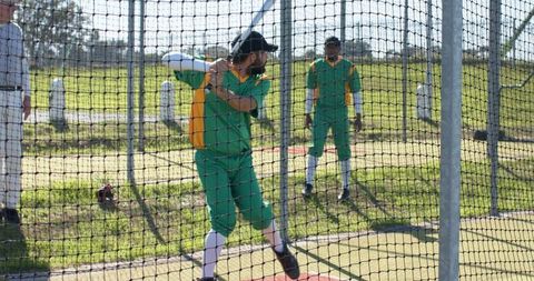 Cricket batsman batting in practice net wearing green-yellow kit during outdoor training