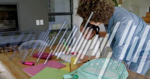 Leaning woman helping child with homework at dining table with mint backpack and supplies