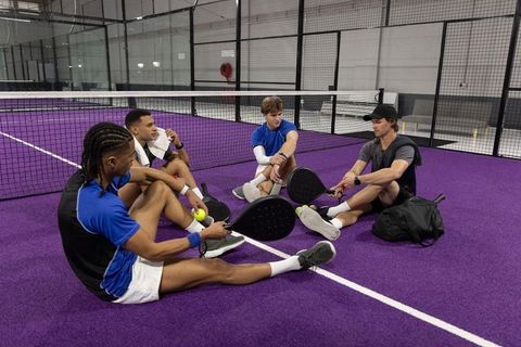Young diverse men resting and planning on purple padel court with rackets and balls