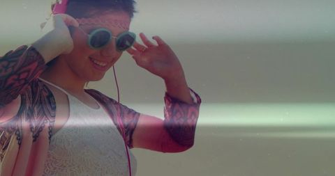 Smiling young woman adjusting wired headphones and sunglasses while enjoying summer music