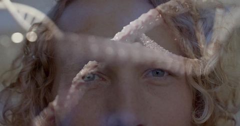 Gazing blond curly man with blue eyes through reflective glass with starfish bokeh overlay
