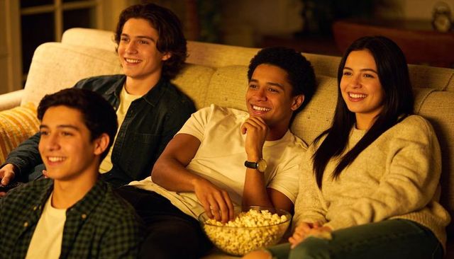 Friends watching movie on couch at home eating popcorn cozy evening gathering casual denim
