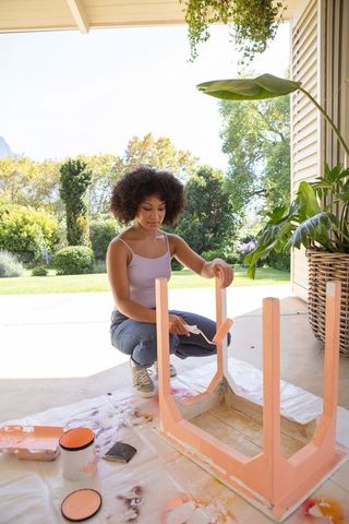 Woman painting side table on patio in bright outdoor setting