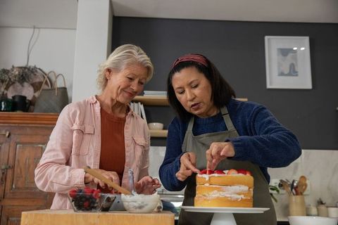 Multigenerational women decorating layered strawberry cake in cozy kitchen, baking together