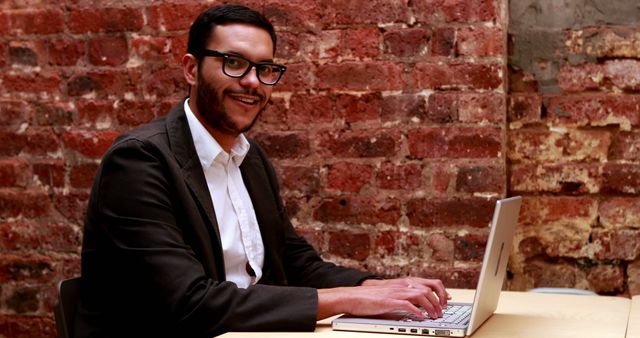 Smiling Man Working on Laptop in Brick Wall Office - Download Free Stock Images Pikwizard.com