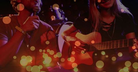 Live acoustic duo singing and strumming on moody club stage with warm bokeh lights