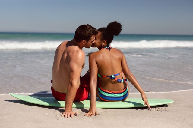 Young couple kissing each other while sitting on surfboard at beach in the sunshine - Download Free Stock Photos Pikwizard.com