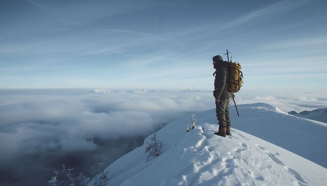Solo hiker surveying alpine summit above cloud inversion with yellow backpack and ice axe