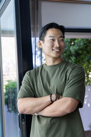 Asian man standing smiling with arms crossed in casual green shirt at patio doorway