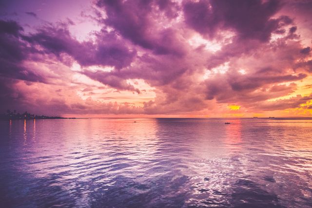 Capturing a mesmerizing tropical sunset, the image showcases a tranquil ocean reflecting the vivid colors of the evening sky. The scene features dramatic clouds against a backdrop of an ethereal horizon. Ideal for promotional materials for travel and tourism, inspirational artwork, nature-themed posters, or background content for websites and social media related to relaxation and vacation.