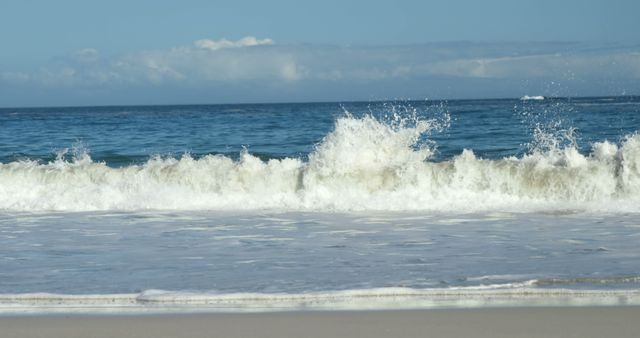 Ocean waves are crashing onto a sandy shoreline under a clear sky. The image showcases the dynamic movement of the waves and the peacefulness of the beach setting. This can be used for travel websites, promoting beach destinations, nature blogs, or wellness advertisements emphasizing serenity and natural beauty.