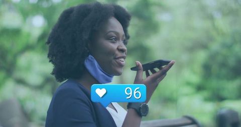 Woman using smartphone with face mask outdoors, displaying like icon