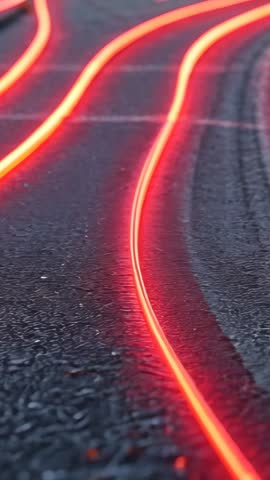 Descending vertical video showing red neon light trails gliding over wet asphalt at night