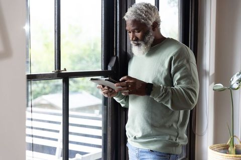 Senior african american man using tablet by sunlit window in relaxed home interior