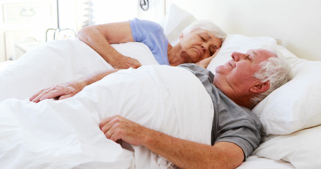 This image depicts an elderly couple sleeping peacefully in bed. They appear relaxed and comfortable, with a serene and loving atmosphere. This picture can be used in advertisements and articles promoting senior health, sleep products, family values, love and relationships, or retirement living.