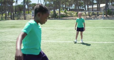 Diverse girls playing soccer on sunlit turf, youth team training outdoors, motion