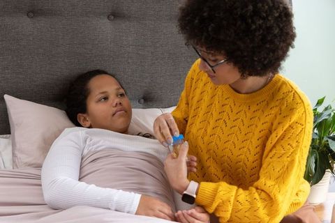 Caregiver giving medicine to child in bed, home nursing and comfort during illness