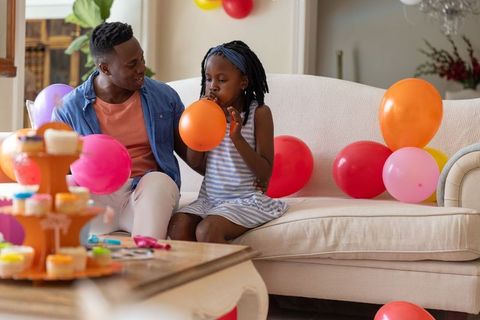 African american father and daughter blowing balloons for home birthday celebration