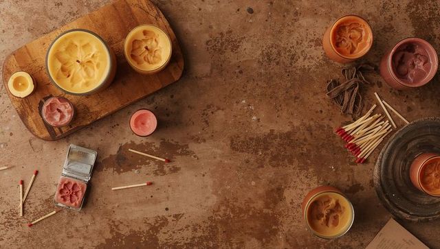 Arranging handmade candles on rustic wooden workbench flatlay with wax tins and matches