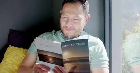 Relaxed senior asian man reading magazine in bright living room