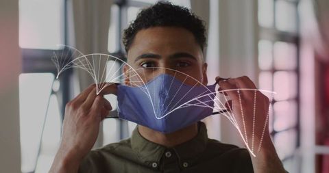Young man putting on blue cloth mask in minimalist office with data overlay
