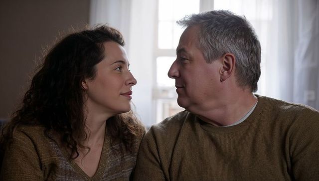 Middle-aged couple sharing intimate moment on couch by window wearing knit sweaters, cozy companions