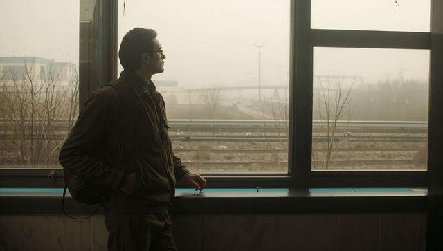 Solitary commuter standing at station window gazing at foggy rail tracks