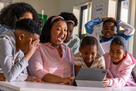 Smiling teacher and elementary students gathering around tablet for interactive learning