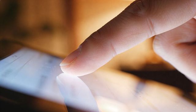 Closeup Finger Tapping Touchscreen Tablet with Reflection, Smudges and Warm Bokeh Lighting