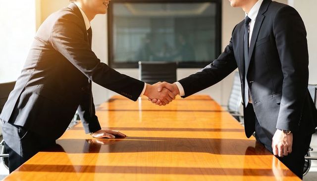 Executives shaking hands over boardroom table signaling partnership and deal closing