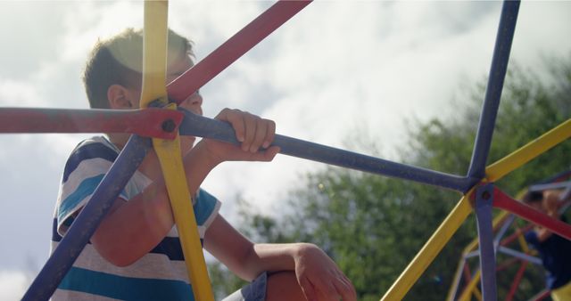 Young boy climbing on a vibrant playground jungle gym, enjoying outdoor activity on a sunny day. Ideal for depicting childhood fun, outdoor play, and physical exercise. Suitable for use in articles about children, parenting, and active lifestyles.