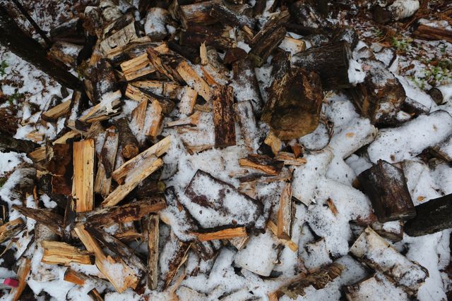 Pile of firewood is covered in snow during the winter season, emphasizing the contrast between the warmth of the wood and the coldness of snow. This visual can be used in articles or blogs about seasonal changes, preparing for winter, nature, or outdoor activities. It also serves well in educational material about resource preparedness and eco-friendly practices.