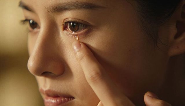 Intimate close-up asian woman touching tear on lower eyelid with fingertip, vulnerable emotion