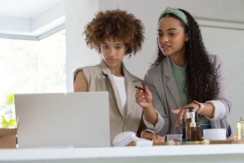 African american entrepreneurs collaborating over laptop and skincare products in bright studio