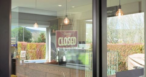 Female barista standing behind counter displaying closed sign at rustic cafe with outdoor patio