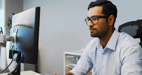 Focused professional man working at widescreen monitor on modern ergonomic office desk